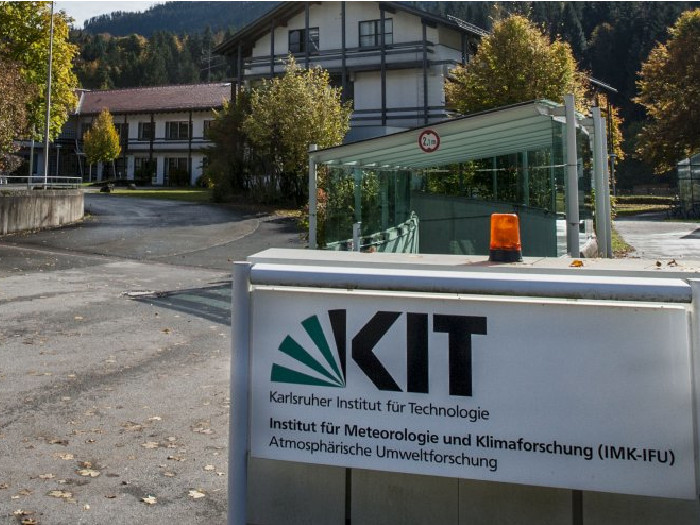 Sign outside KIT institute building with logo and a guard barrier near a glass entrance.