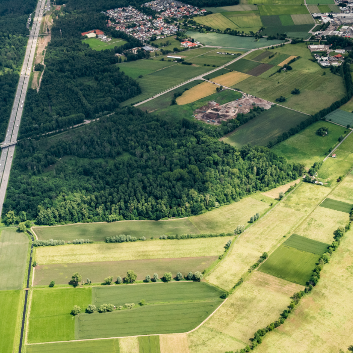 Aerial view of highway passing through forest and agricultural fields with rural buildings.